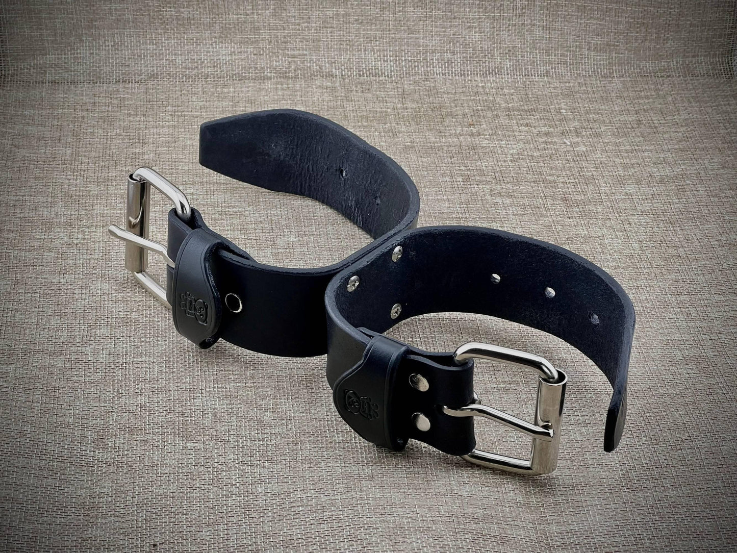 Black leather cuffs with silver buckle on a textured beige background
