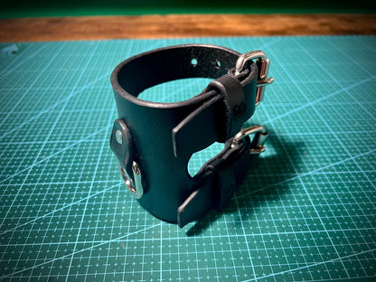 Black leather cuff with metal clasps on a green cutting mat