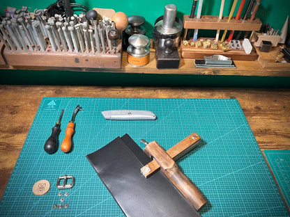 Workbench with leatherworking tools and materials on a green cutting mat.