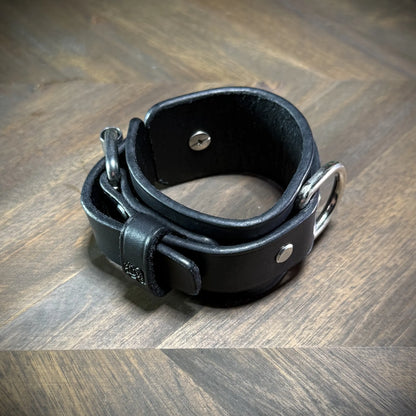 Side profile curvature view of an unbuckled two-piece black leather wristband demonstrating the thickness of the 8oz vegetable-tanned hide.