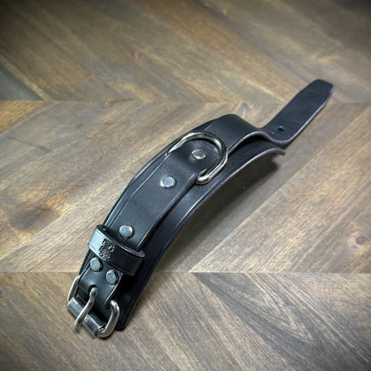 Flat profile view of an unbuckled 1.75" black leather cuff highlighting the heavy dual-layer strap construction and central steel D-ring.