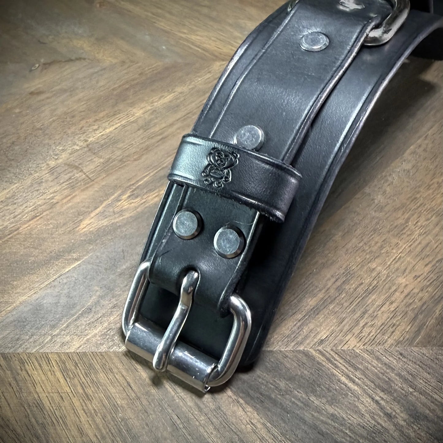 Close macro view of a 1.75" black leather strap featuring an embossed clean bear studio logo mark alongside a heavy steel roller buckle.