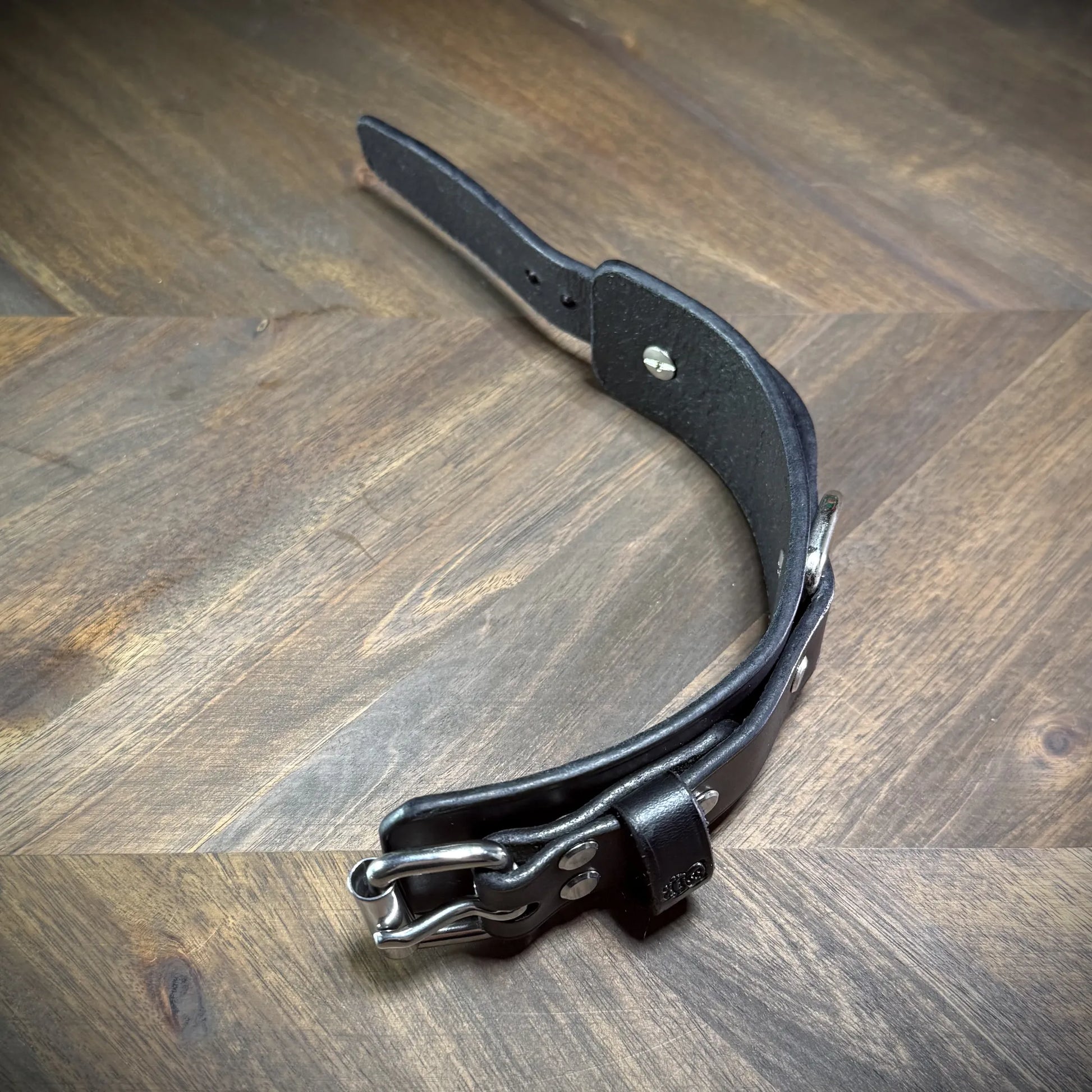 Interior view of a bench-crafted black leather cuff showing smooth burnished edges and secure flush-mounted steel hardware rivets.