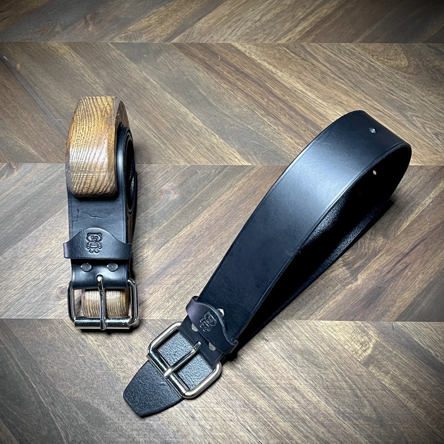 Diagonal view of a pair of Knotty Oso restraints bench-crafted from 8oz vegetable-tanned leather, showcasing the smooth strap and steel dual-prong buckles.