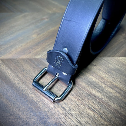 Detail macro of a handcrafted black leather strap focusing on dual structural steel rivets and a clean nickel-plated buckle mechanism.