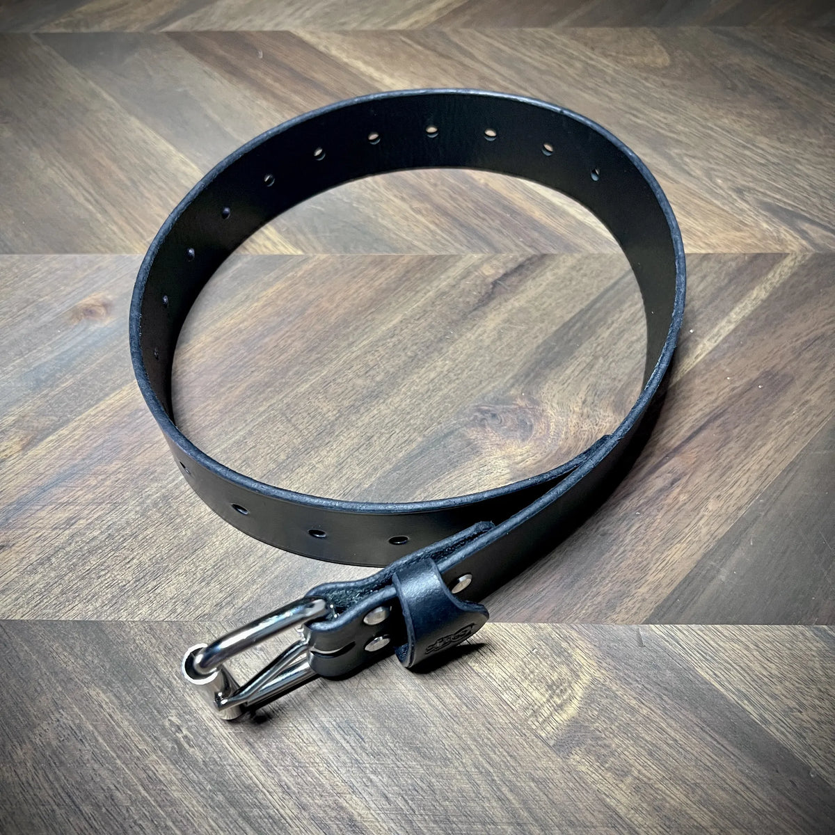 Full product reveal of a 1.5" wide black leather belt formed in a circle showing clean sizing holes punched through premium vegetable-tanned hide.