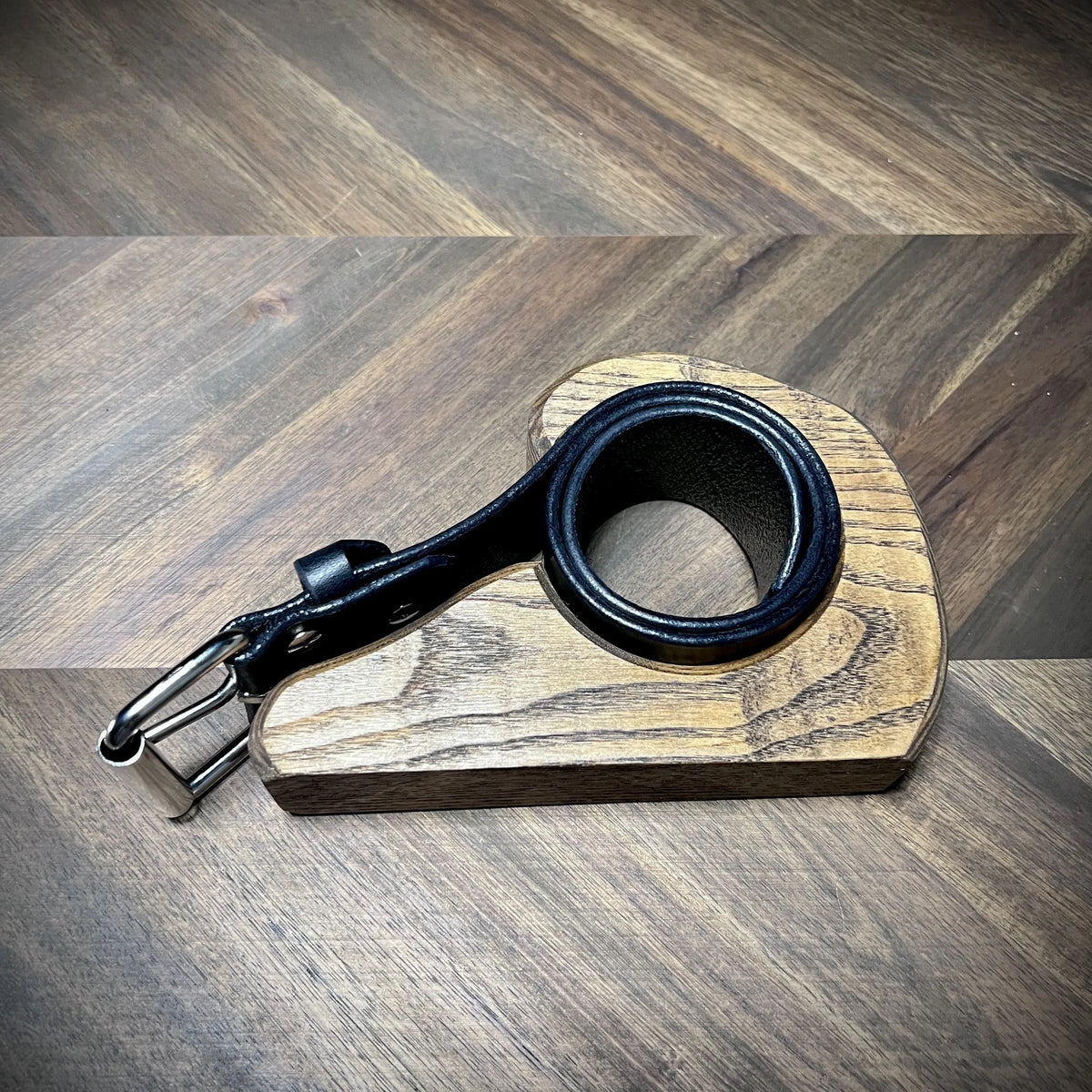Side view of a Knotty Oso 1.75" black leather belt nested in a custom wooden sizing block, highlighting burnished edge details and steel hardware.