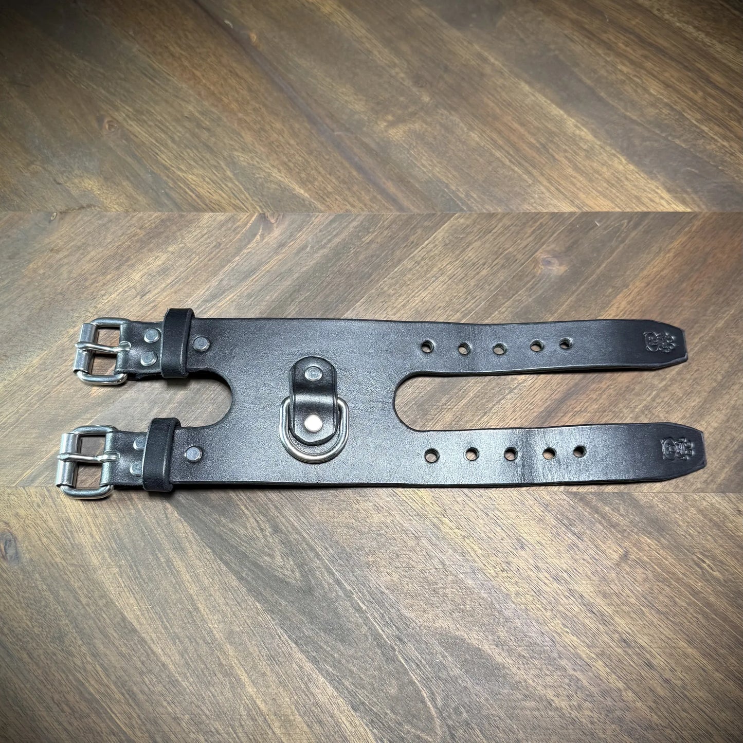 Top view of a handcrafted 3.5" black leather restraint cuff unbuckled flat, featuring nickel-plated steel hardware and a centered D-ring.