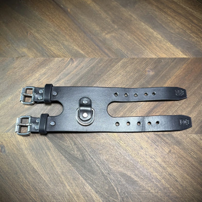 Top view of a handcrafted 3.5" black leather restraint cuff unbuckled flat, featuring nickel-plated steel hardware and a centered D-ring.