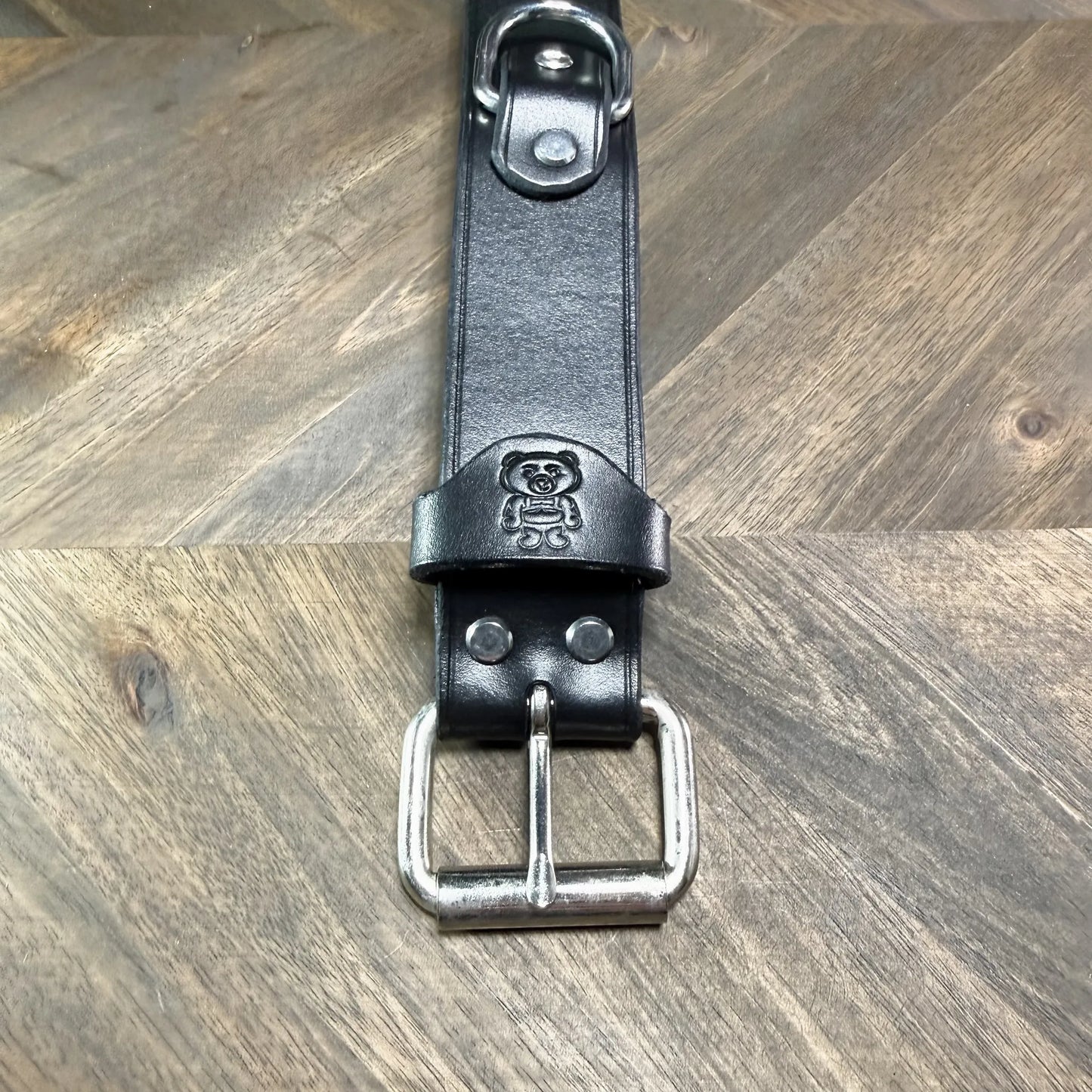 Macro view of the steel roller buckle attachment on a 1.5" black leather cuff, showing dual hardware rivets and a clean strap keeper loop.