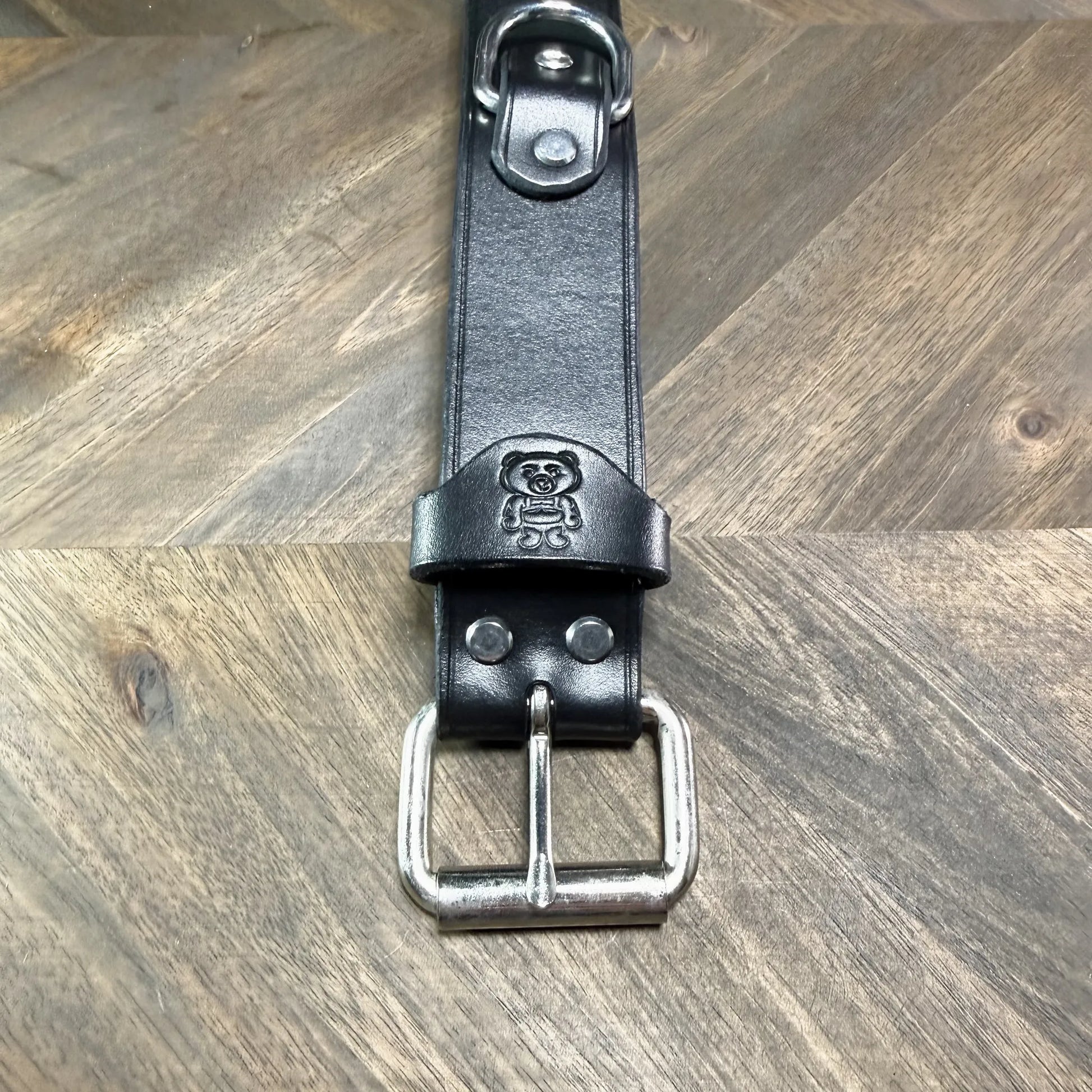 Macro view of the steel roller buckle attachment on a 1.5" black leather cuff, showing dual hardware rivets and a clean strap keeper loop.