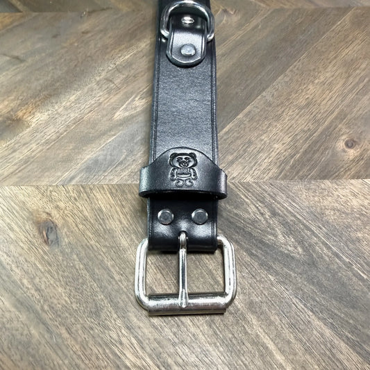Macro view of the steel roller buckle attachment on a 1.5" black leather cuff, showing dual hardware rivets and a clean strap keeper loop.
