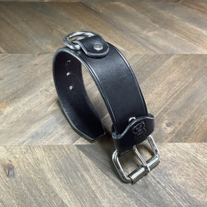 Rear perspective view of a buckled 1.5" black leather cuff highlighting a heavy-duty nickel-plated steel D-ring secured by a leather overlay.