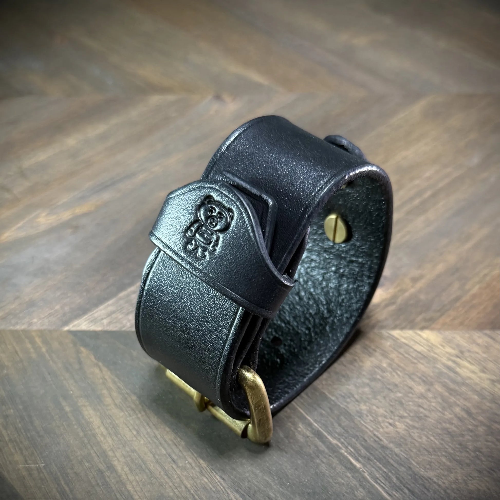 Three-quarter isometric view of a handcrafted 1.5" leather cuff showcasing premium black leather, solid brass roller buckle, and burnished edges styled as a minimalist subculture accessory.