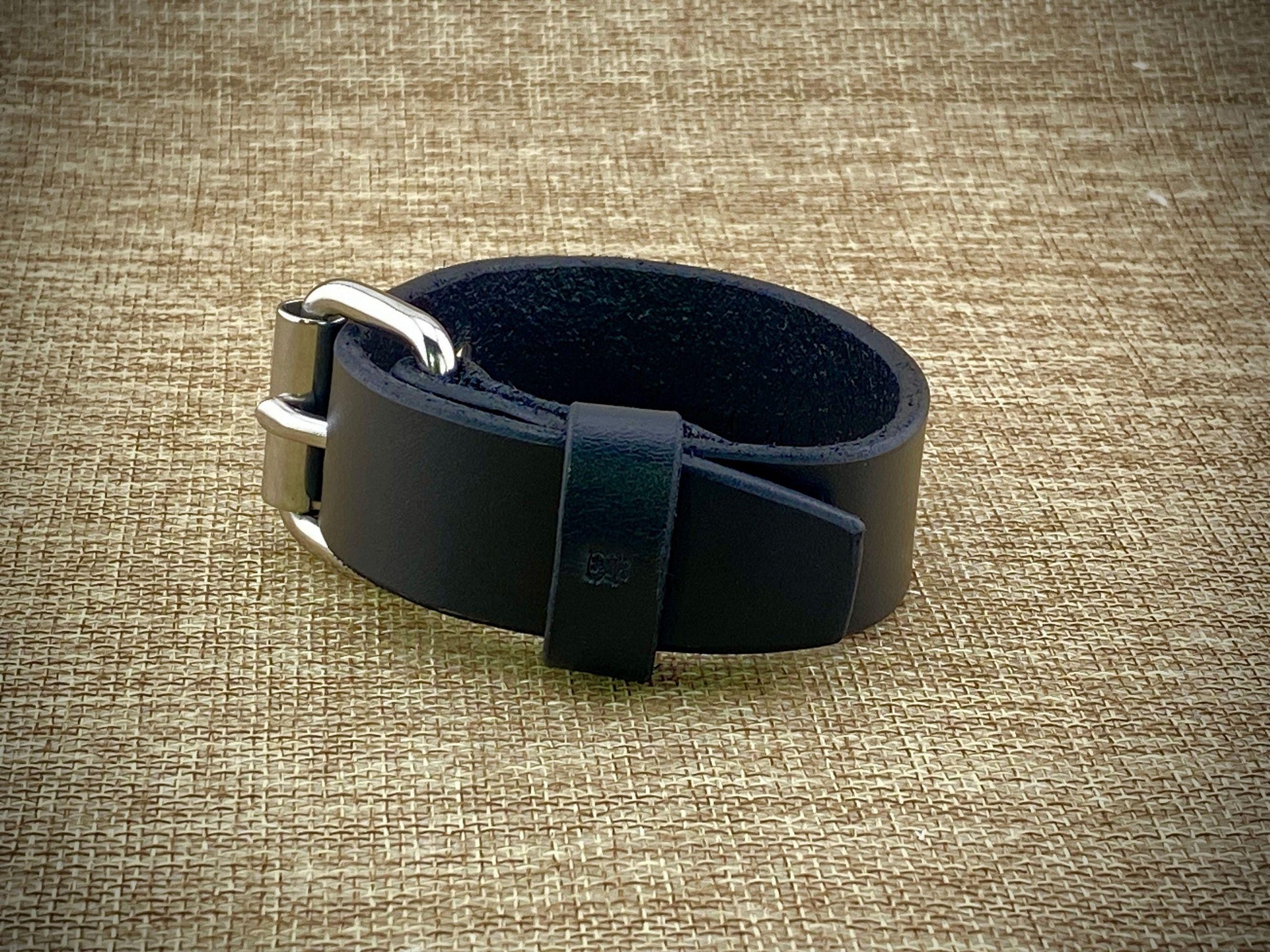 Detail macro view of a handcrafted 1" wrist cuff showcasing factory dyed and finished on both sides leather, steel buckle closure, and precise adjustment hole spacing