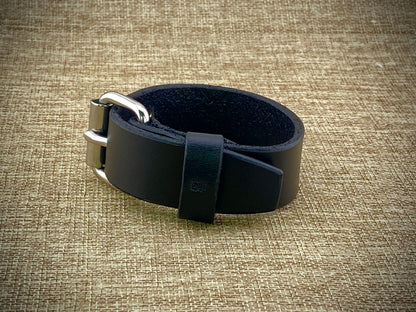 Detail macro view of a handcrafted 1" wrist cuff showcasing factory dyed and finished on both sides leather, steel buckle closure, and precise adjustment hole spacing