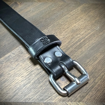 Detail-macro view of a black leather cuff buckle section, emphasizing dual steel anchoring rivets and an embossed maker mark on the keeper.