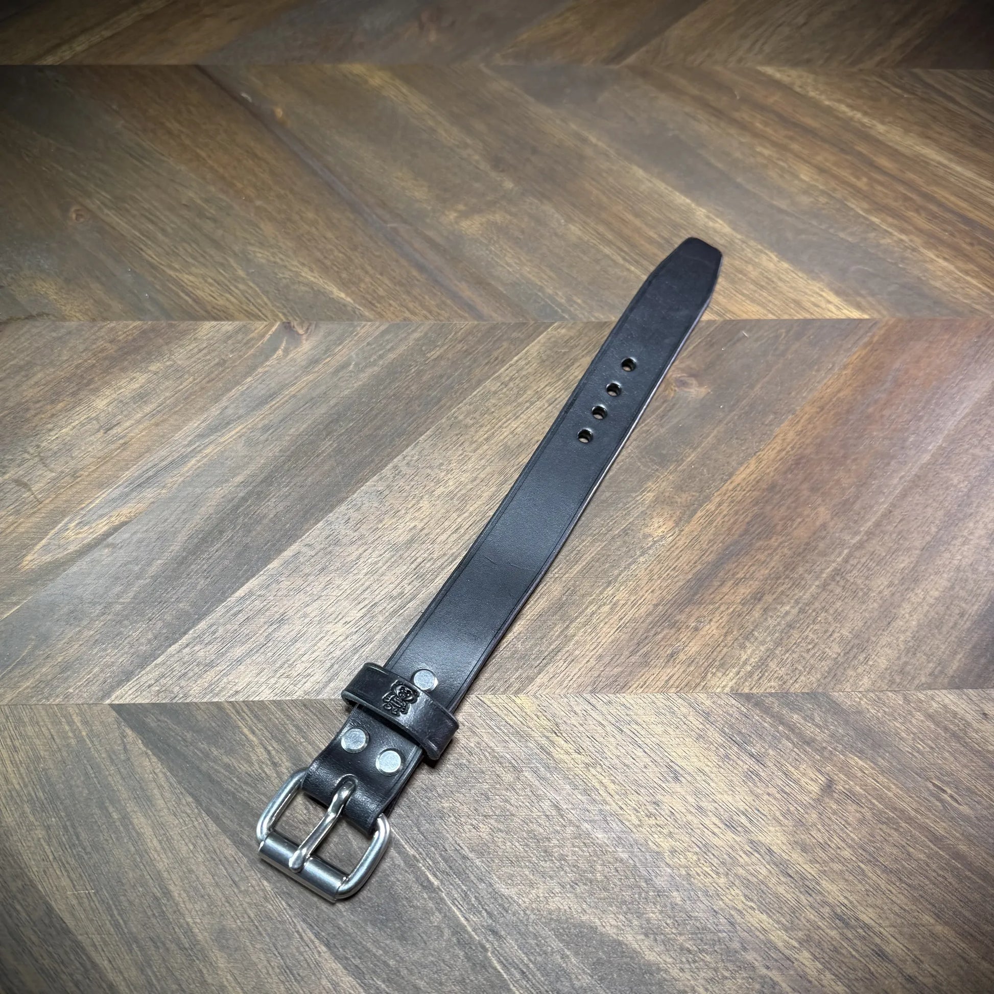 Hero-tilt view of a handcrafted 1.0" leather wrist cuff showcasing premium black cowhide, nickel-plated steel buckle, and burnished edges.