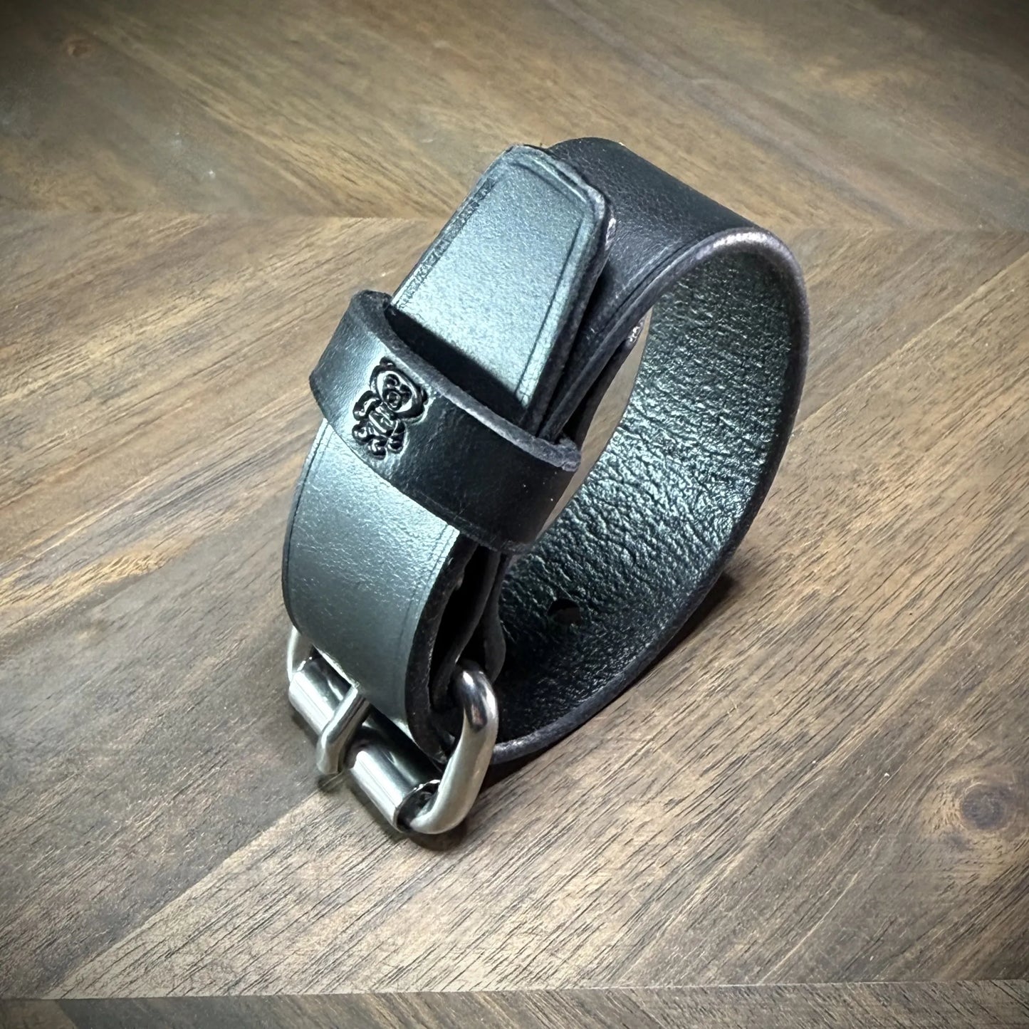 Detail-macro view of a rolled 1.0" black leather band showing the textured flesh side, rounded buckle tip, and finished edge alignment.