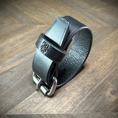 Detail-macro view of a rolled 1.0" black leather band showing the textured flesh side, rounded buckle tip, and finished edge alignment.