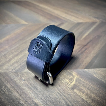 Hero tilt view of a handcrafted 1.25" black leather wrist cuff showcasing its structured circular form and smooth hand-burnished edges.