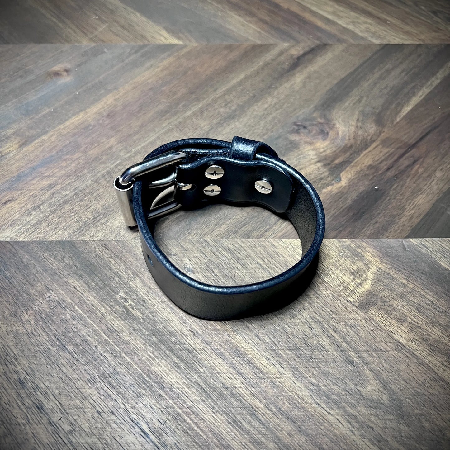 Product profile view of a buckled 1.25" black leather wrist cuff showcasing flush interior fasteners and a clean leather interior finish.