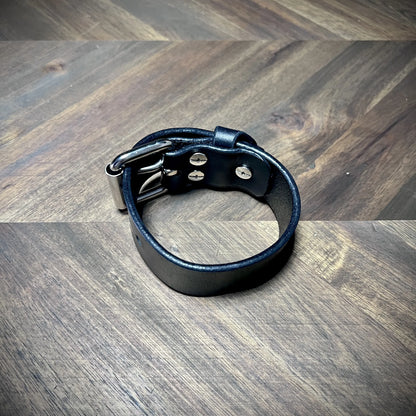 Product profile view of a buckled 1.25" black leather wrist cuff showcasing flush interior fasteners and a clean leather interior finish.