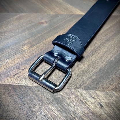 Detail macro view of the debossed bear logo and reinforced dual-rivet construction near the steel buckle of a 1.5" black leather cuff.