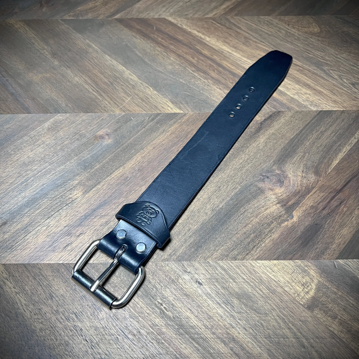 Hero tilt of a handcrafted 1.5" black leather wrist cuff showcasing premium vegetable-tanned hide with a nickel-plated steel roller buckle.
