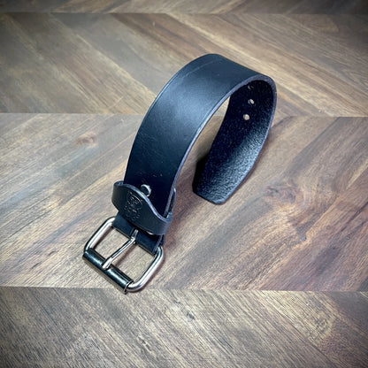 Three-quarter curve view of a 1.5" black leather wrist cuff, displaying its rigid structural form and smooth hand-burnished edges.