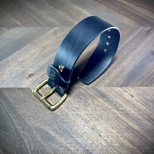 Product reveal view of a coiled 1.5" black leather cuff showcasing robust 8oz vegetable-tanned leather density and solid brass closure.