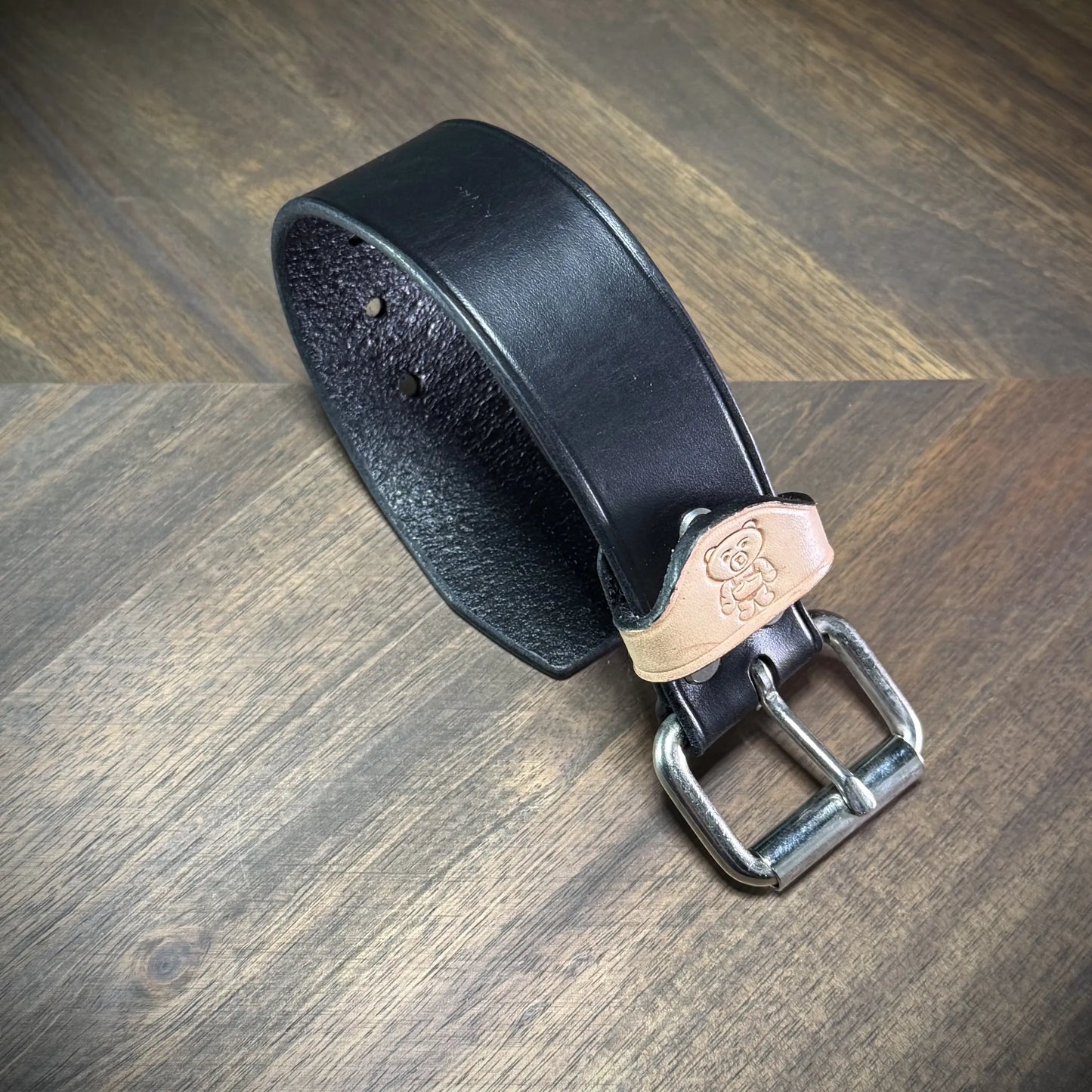 Angled view of a handcrafted 1.5" black and natural leather wrist cuff showcasing premium vegetable-tanned cowhide and steel hardware components.