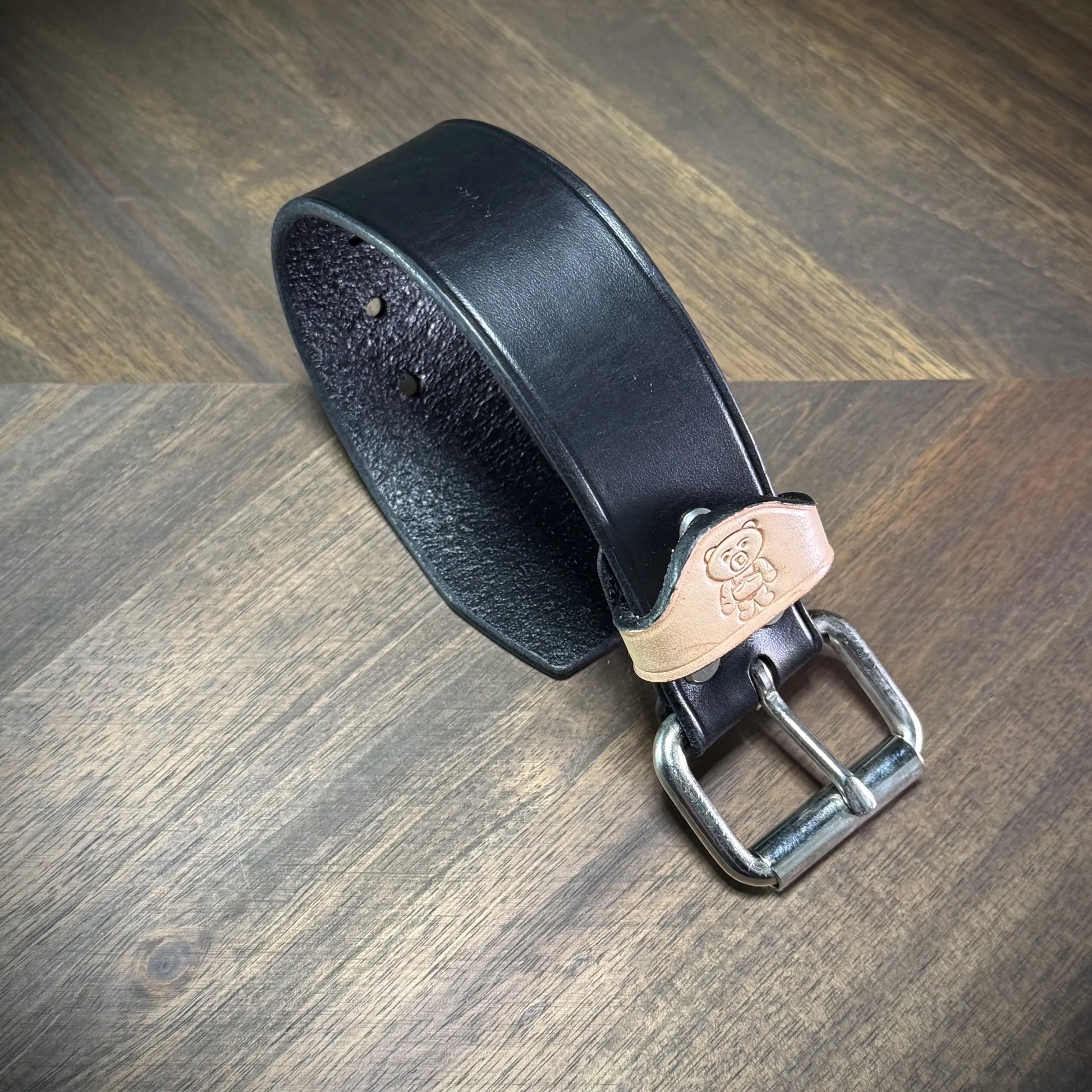Angled view of a handcrafted 1.5" black and natural leather wrist cuff showcasing premium vegetable-tanned cowhide and steel hardware components.