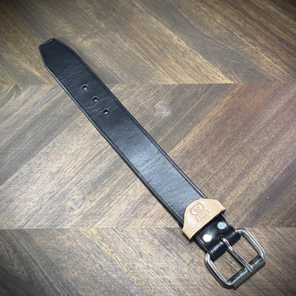Top-down view of a handcrafted 1.5" black and natural leather wrist cuff showcasing premium vegetable-tanned cowhide and steel hardware.