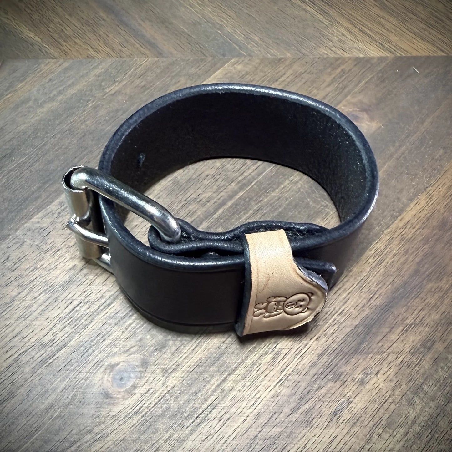 Reverse perspective view of a handcrafted 1.5" black and natural leather wrist cuff showcasing burnished edge finishes and steel buckle.