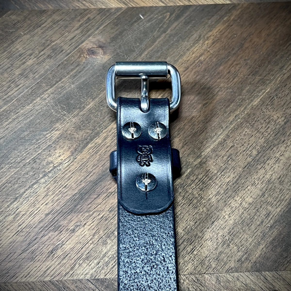 Detail-macro view of a handcrafted 1" black leather wrist cuff showcasing premium vegetable-tanned leather, steel buckle, and bear logo detail.