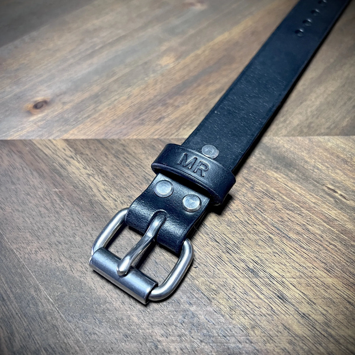 Macro close-up of a black leather cuff highlighting steel rivet alignment and durable strap loop engineering.