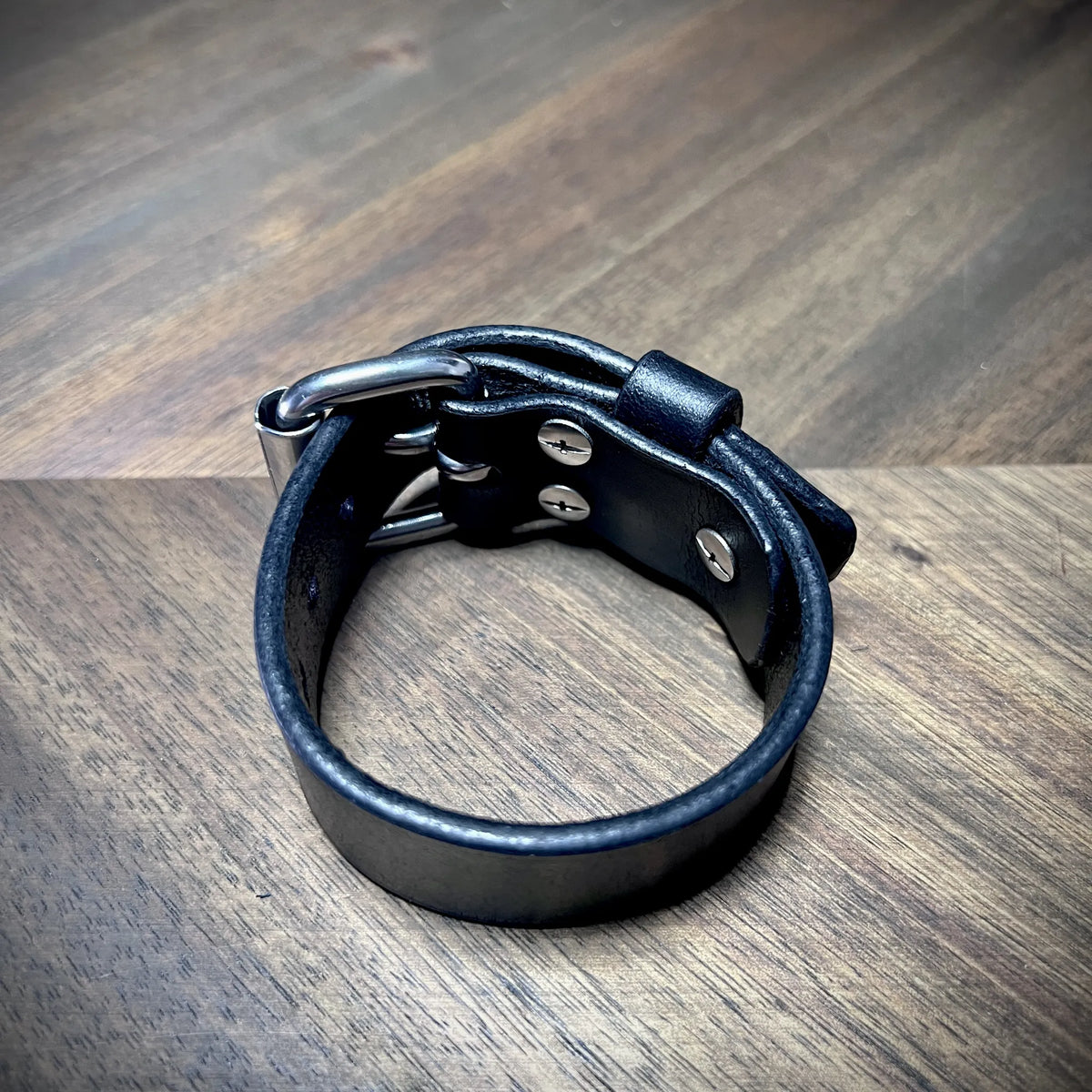 Interior reverse angle view of a black leather cuff revealing secure steel hardware fasteners and smooth burnished edges.
