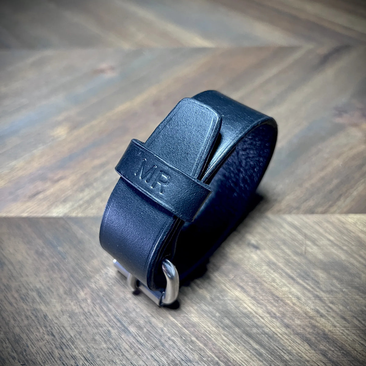 Side perspective profile of a buckled black leather wristband displaying solid edge alignment and curved structural form.