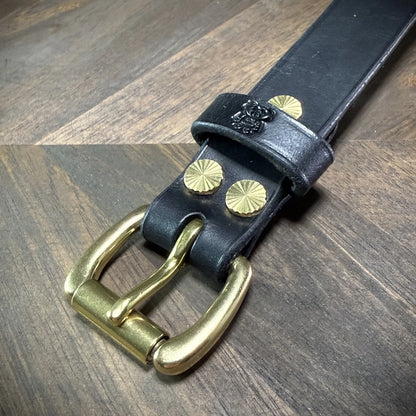Macro view highlighting the solid brass buckle, debossed bear logo keeper, and dual sunburst brass Chicago screws on a black leather cuff.