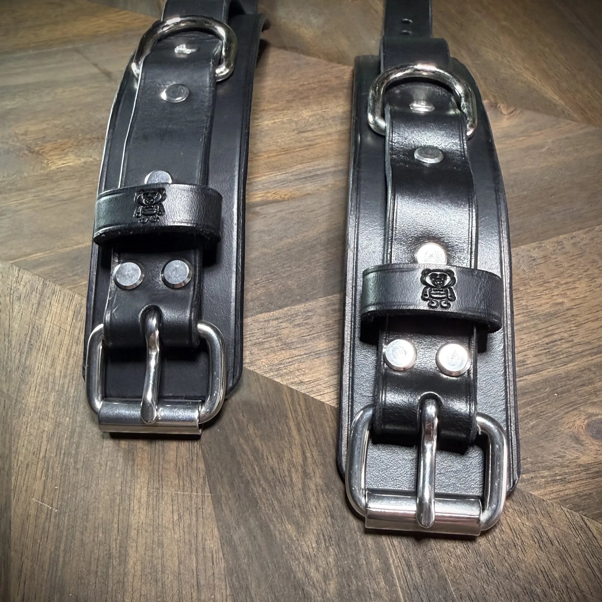 Macro close-up structural detail of heavy double-pronged nickel-plated steel roller buckles securely riveted into thick 8oz full-grain black leather.