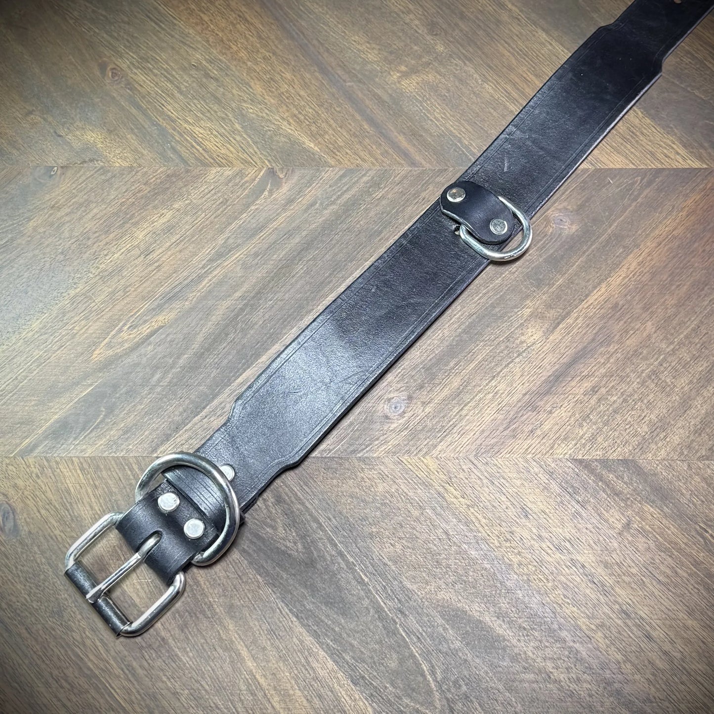 Top-down flat view of a 1.75" black leather collar revealing the full strap layout, roller buckle, belt keeper, and anchored D-ring.