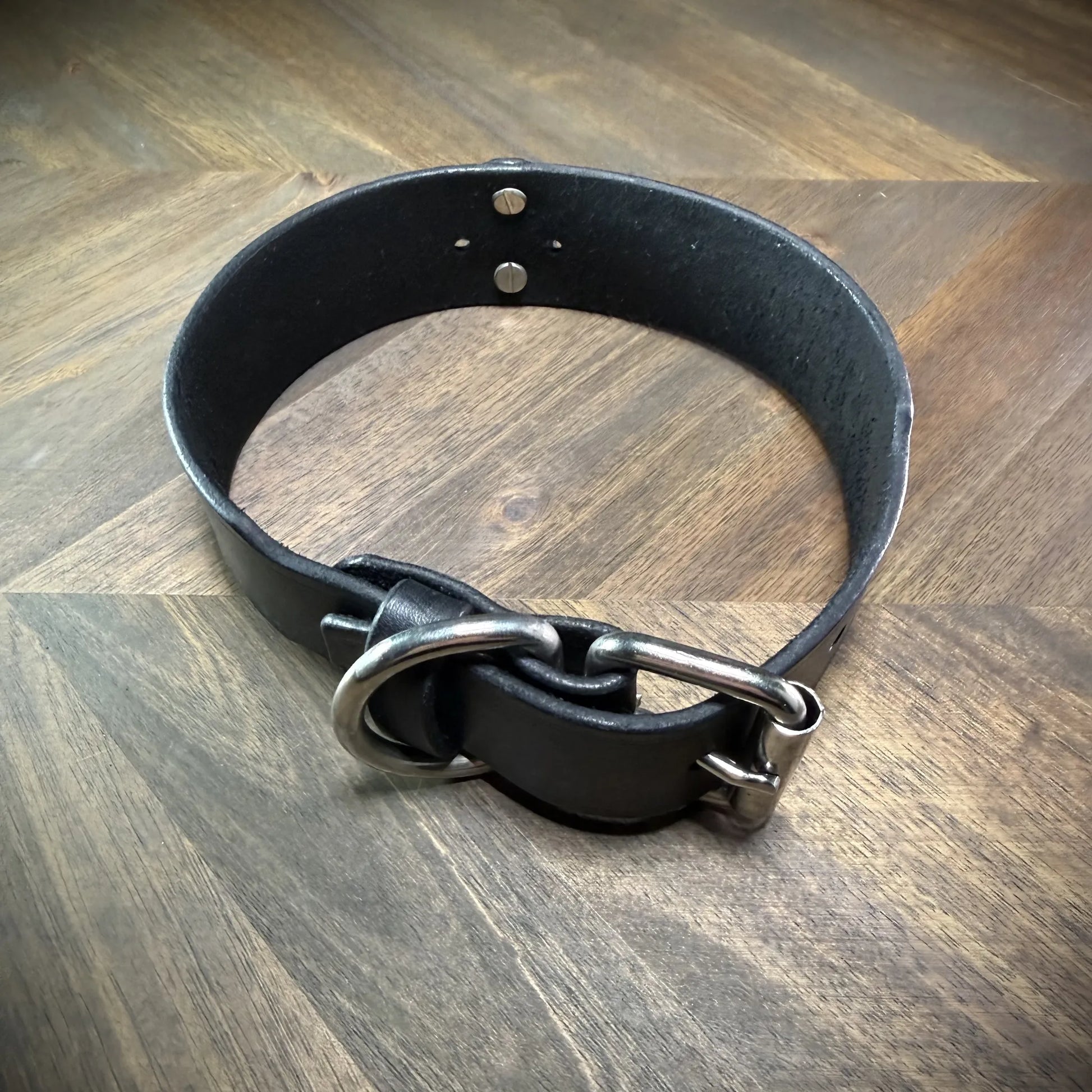 Hero-tilt view of a handcrafted 1.75" black leather collar featuring premium vegetable-tanned cowhide and nickel-plated steel hardware.