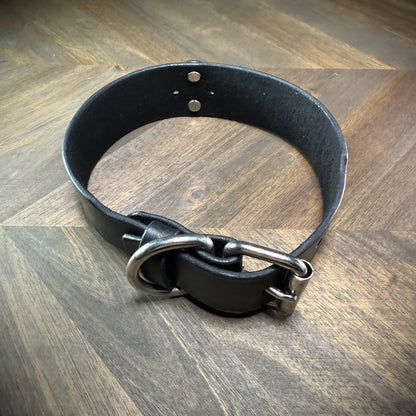 Hero-tilt view of a handcrafted 1.75" black leather collar featuring premium vegetable-tanned cowhide and nickel-plated steel hardware.