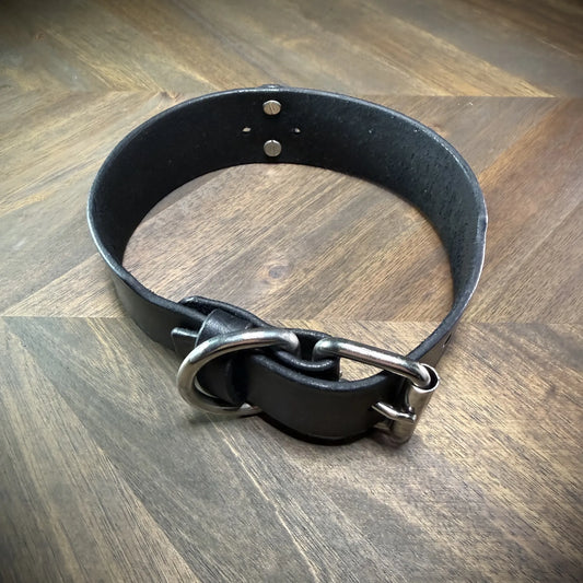 Hero-tilt view of a handcrafted 1.75" black leather collar featuring premium vegetable-tanned cowhide and nickel-plated steel hardware.