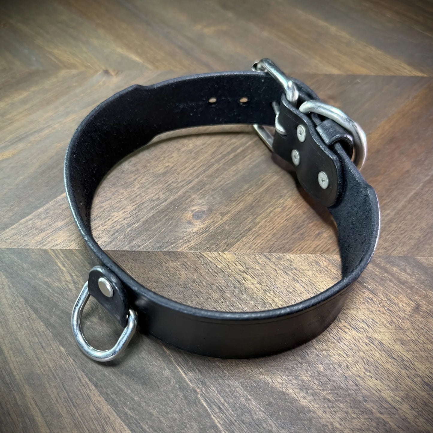 Hero-tilt view of a handcrafted 1.75" black leather collar featuring premium vegetable-tanned cowhide and nickel-plated steel hardware.