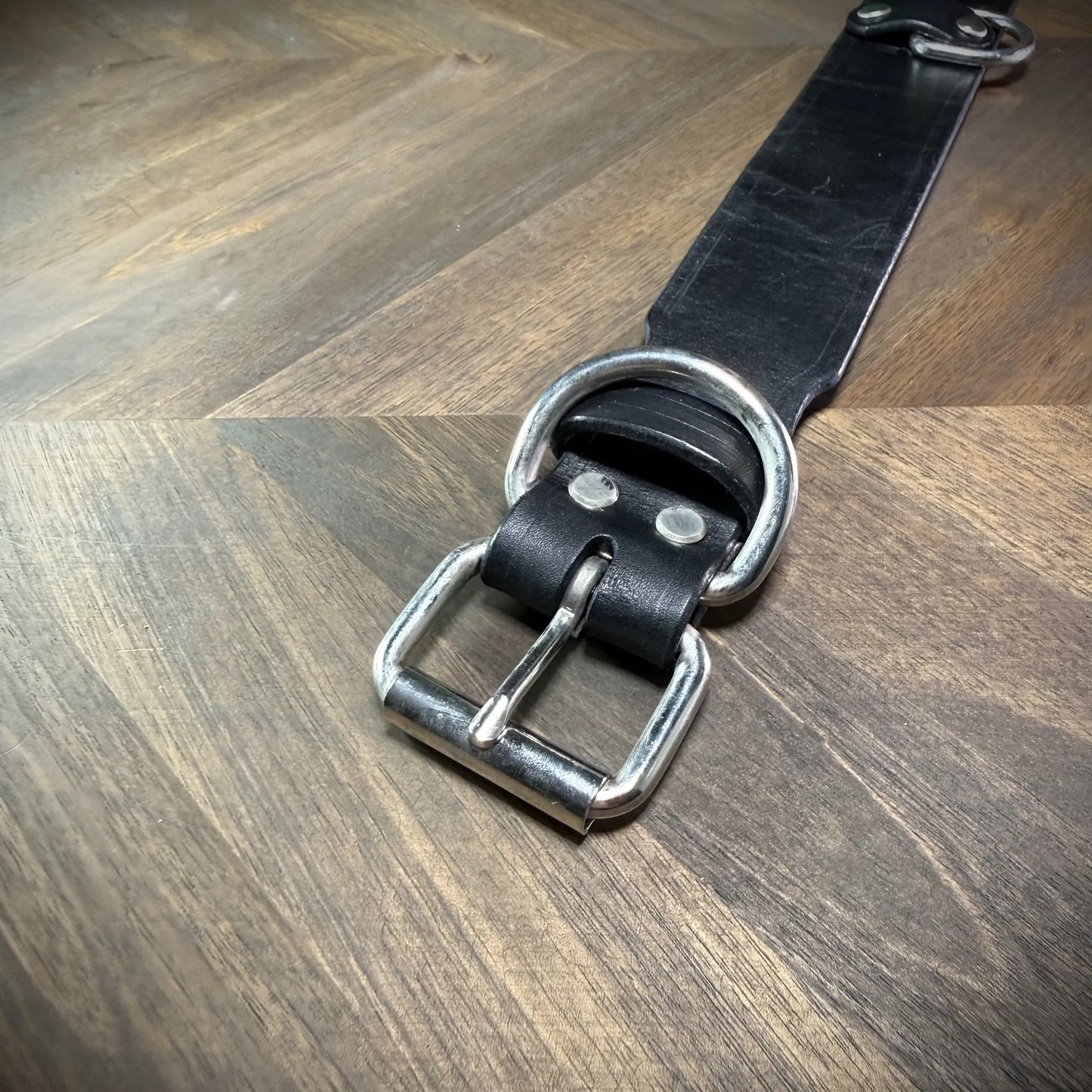 Top-down flat view of a 1.75" black leather collar revealing the full strap layout, roller buckle, belt keeper, and anchored D-ring.