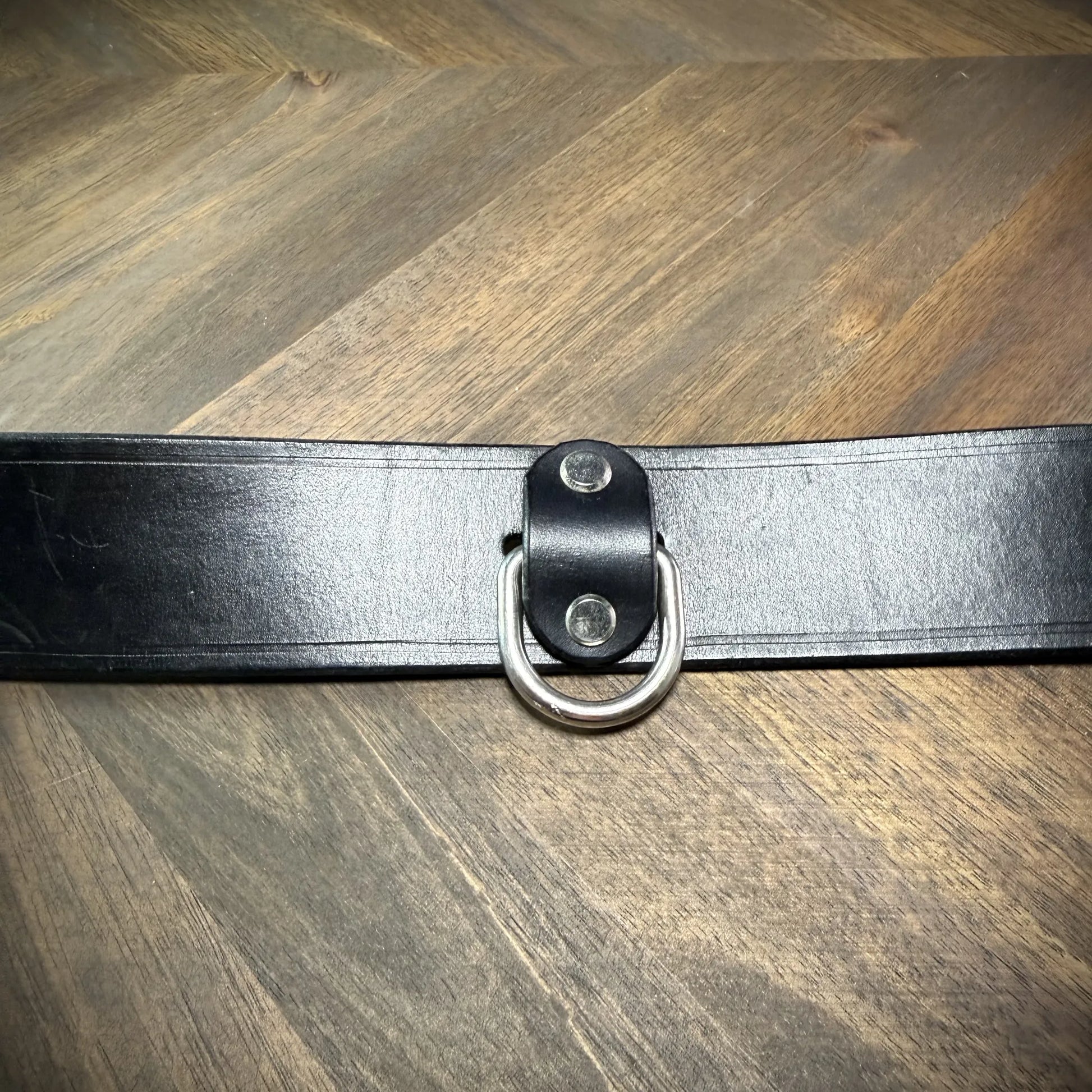 Detail-macro view of a 1.75" black leather collar focusing on the nickel-plated steel roller buckle assembly and burnished leather edge.