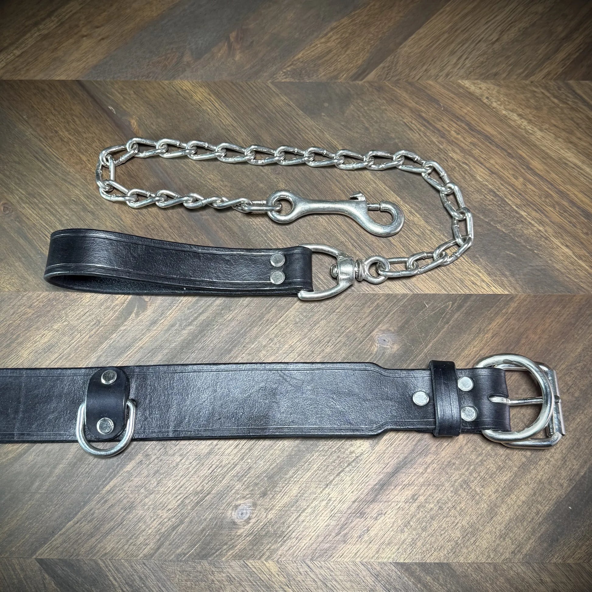 Detail-macro view focusing on the hand-burnished edges, nickel-plated steel buckle, and anchored D-ring of a black leather collar.