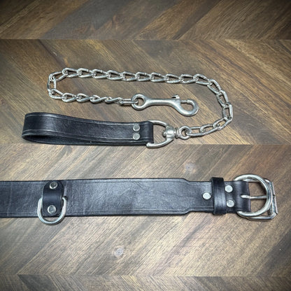 Detail-macro view focusing on the hand-burnished edges, nickel-plated steel buckle, and anchored D-ring of a black leather collar.
